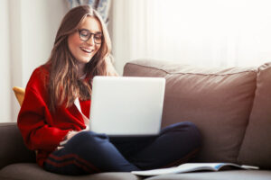 woman seated on couch smiling at laptop