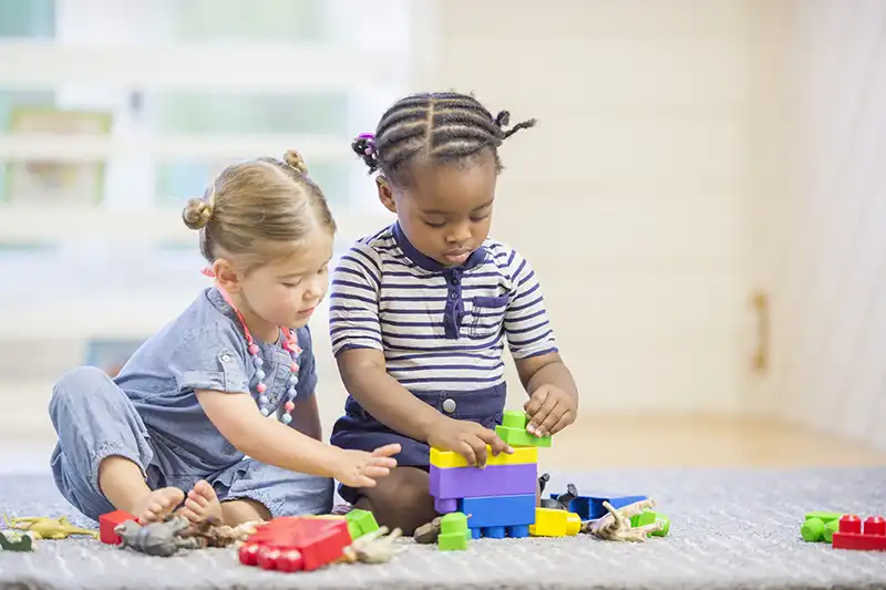 two pre-K toddlers playing with blocks